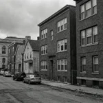 Urban residential street with For Rent signs on brick apartment buildings and city hall visible in background