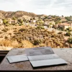 Insurance non-renewal letter on desk with California hillside visible, representing STR insurance denied markets 2026